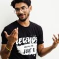 South Asian man wearing eyeglasses and a printed t-shirt posing casually in Varanasi, India.