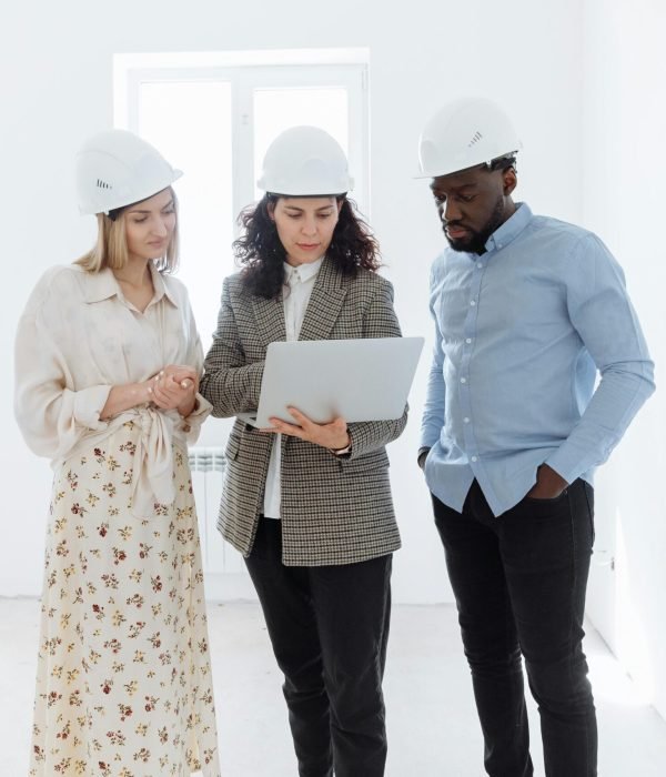 pexels-photo-8470060-8470060 Three professionals in hard hats examining floor plans on a laptop indoors.